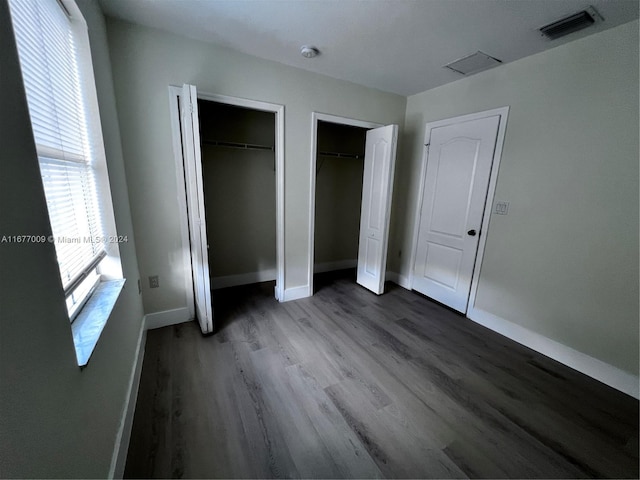 unfurnished bedroom with multiple windows, hardwood / wood-style flooring, and two closets