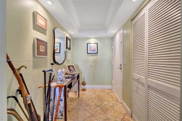 hallway featuring a tray ceiling, ornamental molding, and light tile patterned floors