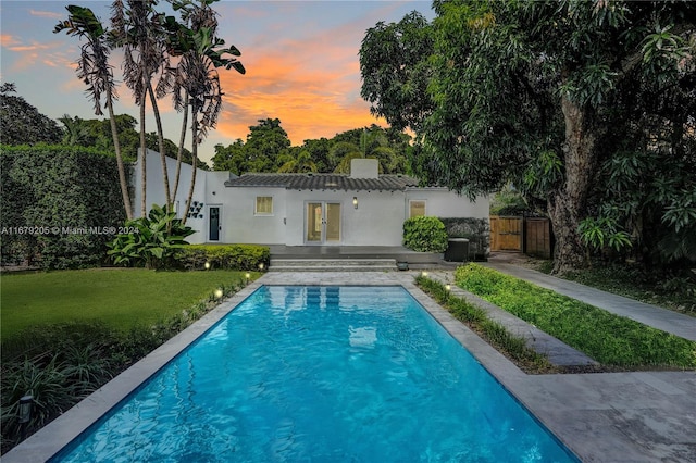 pool at dusk with french doors, a patio, and a lawn