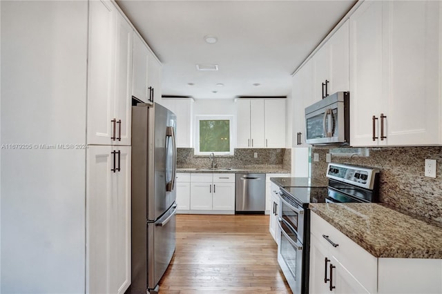 kitchen featuring appliances with stainless steel finishes, sink, stone countertops, white cabinetry, and light hardwood / wood-style flooring