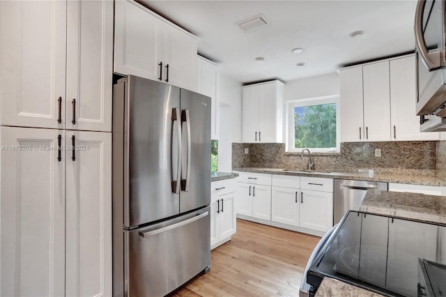 kitchen featuring white cabinets, appliances with stainless steel finishes, light stone countertops, light hardwood / wood-style flooring, and sink