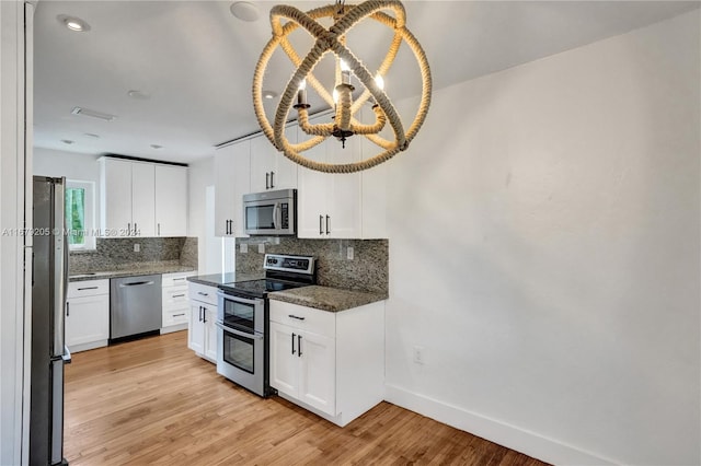 kitchen with appliances with stainless steel finishes, light hardwood / wood-style flooring, white cabinetry, and dark stone counters