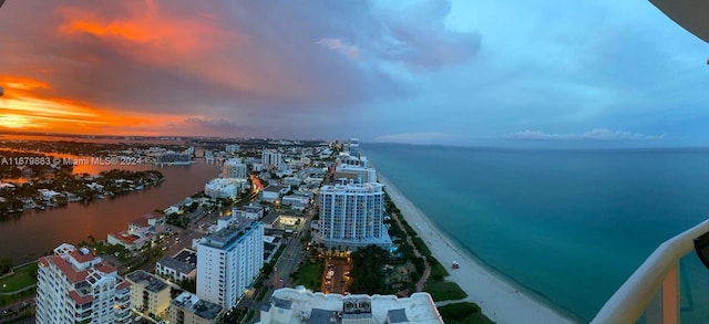 aerial view at dusk featuring a water view and a beach view