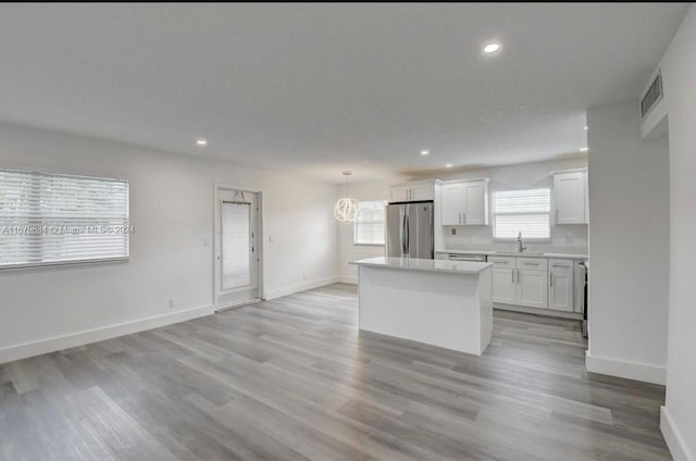 kitchen with a kitchen island, hanging light fixtures, white cabinetry, stainless steel refrigerator, and light hardwood / wood-style flooring