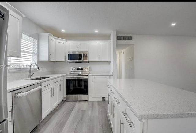 kitchen featuring stainless steel appliances, sink, light stone countertops, white cabinets, and light hardwood / wood-style floors