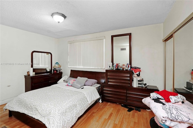 bedroom with a closet, a textured ceiling, and light wood-type flooring