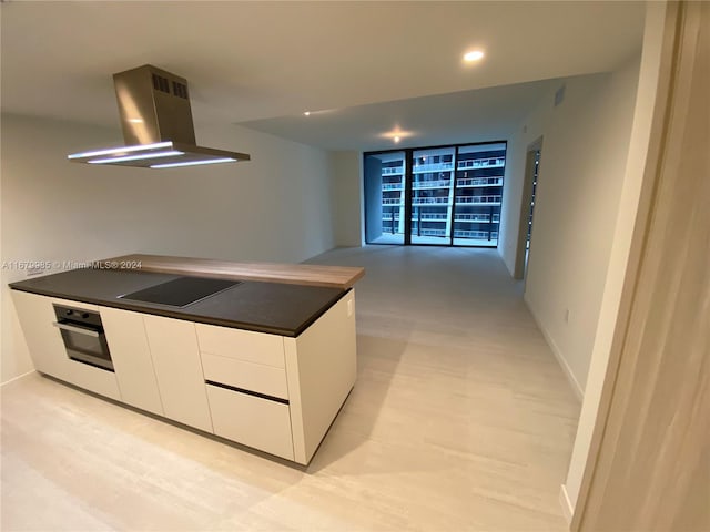 kitchen featuring stainless steel oven, extractor fan, white cabinetry, light wood-type flooring, and black electric stovetop