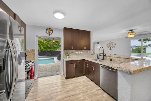 kitchen with kitchen peninsula, light stone counters, appliances with stainless steel finishes, light hardwood / wood-style flooring, and sink