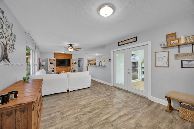 living room featuring french doors, ceiling fan, a textured ceiling, and light wood-type flooring