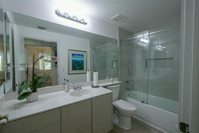 full bathroom with shower / bath combination with glass door, toilet, hardwood / wood-style floors, vanity, and a textured ceiling