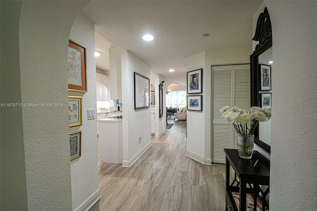 hallway with a textured ceiling and light hardwood / wood-style flooring