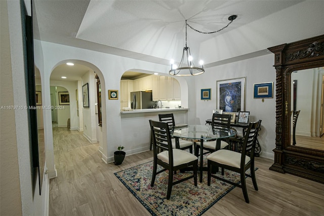 dining room with sink, a textured ceiling, light hardwood / wood-style flooring, and a chandelier