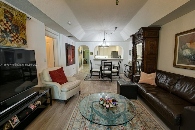 living room with vaulted ceiling, light hardwood / wood-style flooring, and an inviting chandelier