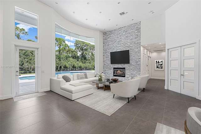 living room with a stone fireplace, a high ceiling, and dark tile patterned floors