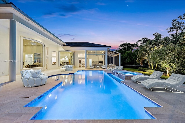 pool at dusk featuring an in ground hot tub and a patio area