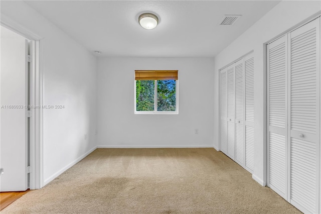 unfurnished bedroom featuring light carpet and multiple closets