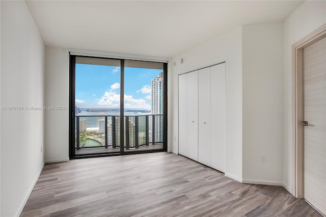 unfurnished bedroom featuring floor to ceiling windows, a closet, light hardwood / wood-style floors, and access to outside