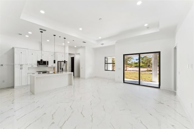 kitchen featuring a kitchen island with sink, white cabinetry, stainless steel appliances, a tray ceiling, and decorative light fixtures