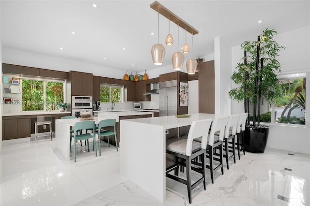 kitchen with wall chimney range hood, a breakfast bar, a center island, dark brown cabinetry, and pendant lighting