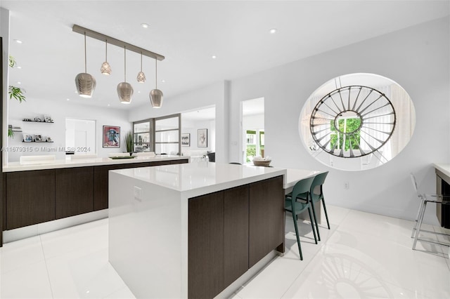 kitchen with a spacious island, dark brown cabinets, light tile patterned flooring, and hanging light fixtures