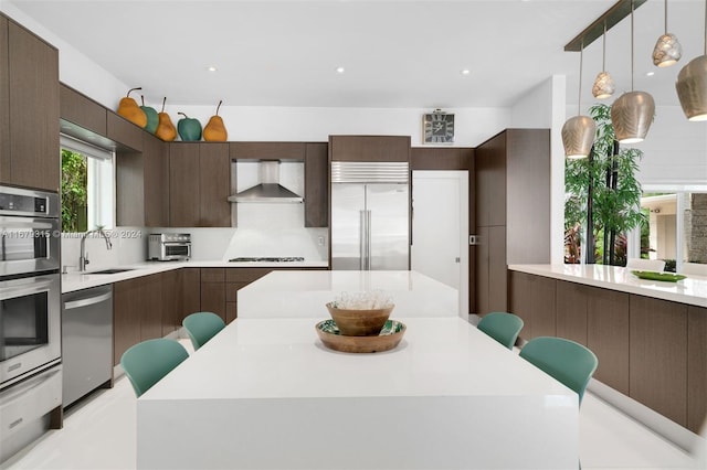 kitchen with sink, wall chimney exhaust hood, appliances with stainless steel finishes, and a breakfast bar area