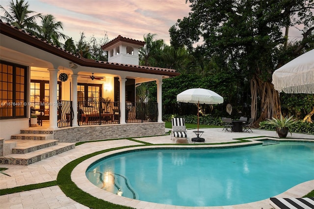 pool at dusk featuring a patio, a ceiling fan, outdoor dining area, an outdoor pool, and french doors