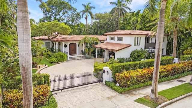 mediterranean / spanish house with stucco siding, driveway, a gate, a fenced front yard, and a tiled roof