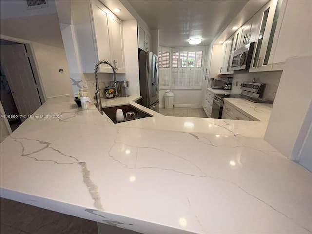 kitchen featuring backsplash, white cabinetry, light stone countertops, sink, and stainless steel appliances