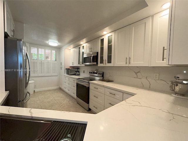 kitchen featuring appliances with stainless steel finishes, decorative backsplash, white cabinetry, and light stone countertops