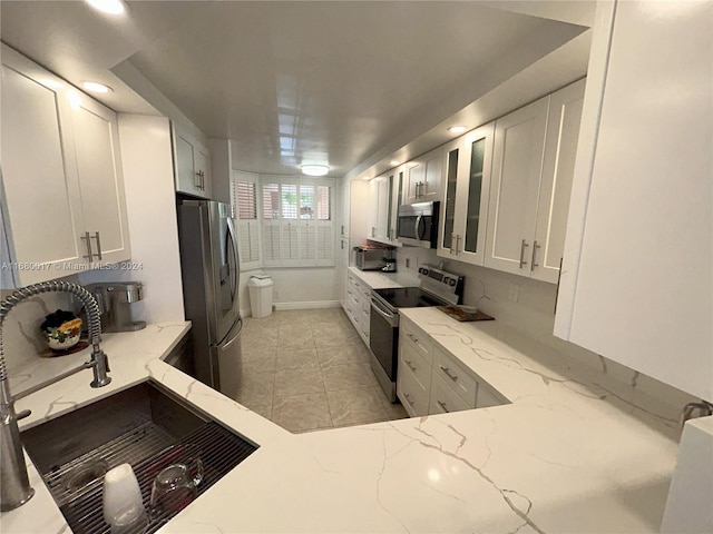 kitchen with white cabinetry, light stone countertops, stainless steel appliances, and sink