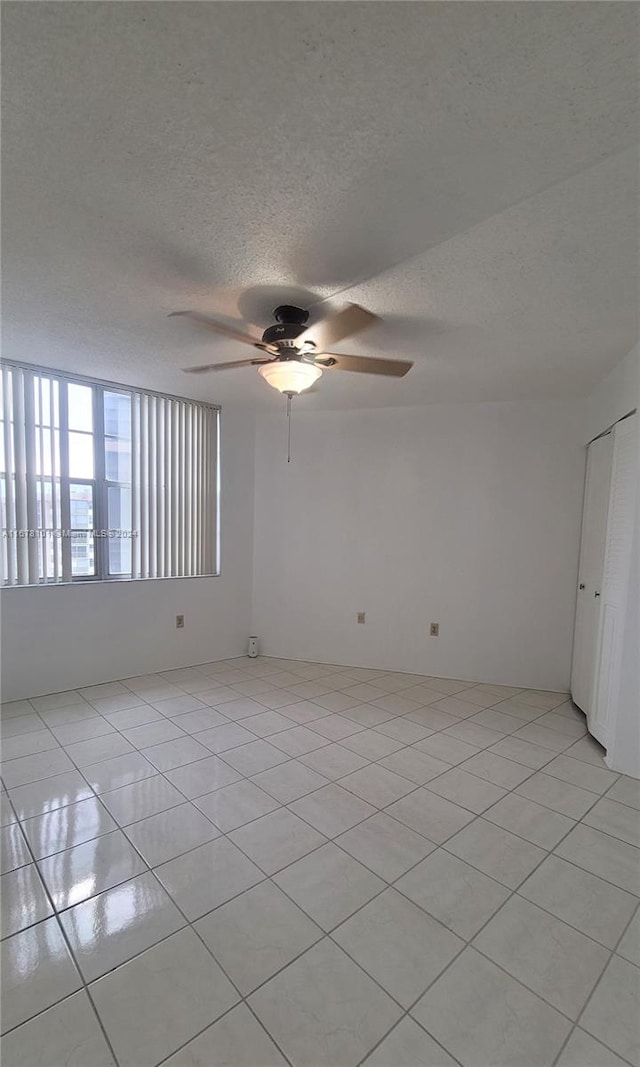 spare room featuring ceiling fan, light tile patterned floors, and a textured ceiling