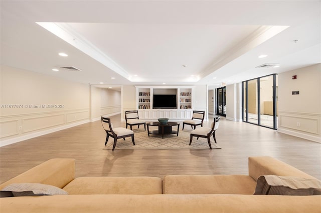 living room featuring built in shelves, light wood-type flooring, crown molding, and a tray ceiling