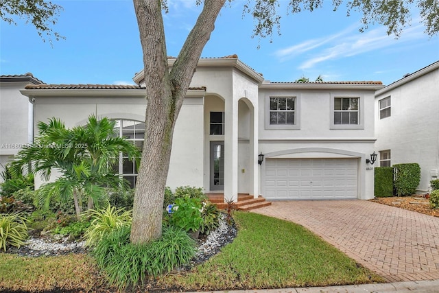 mediterranean / spanish home with a tiled roof, decorative driveway, a garage, and stucco siding