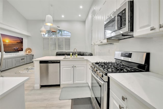 kitchen with kitchen peninsula, appliances with stainless steel finishes, sink, decorative light fixtures, and white cabinets