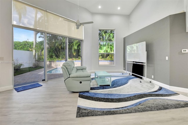 living room featuring plenty of natural light, ceiling fan, light wood-type flooring, and a towering ceiling