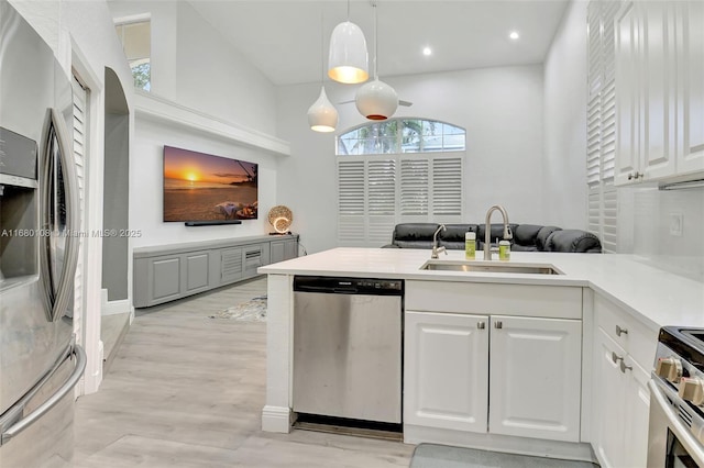 kitchen featuring kitchen peninsula, stainless steel appliances, sink, white cabinets, and hanging light fixtures