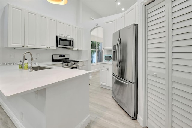 kitchen featuring white cabinets, sink, appliances with stainless steel finishes, light hardwood / wood-style floors, and kitchen peninsula