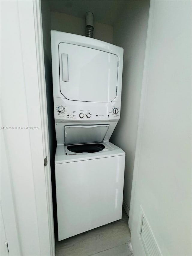 clothes washing area with light hardwood / wood-style floors and stacked washer and clothes dryer