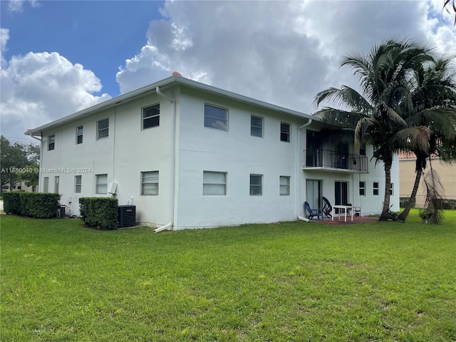 back of property with central air condition unit, a yard, and a balcony