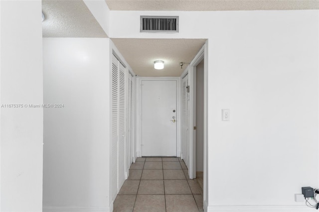 corridor with a textured ceiling and light tile patterned flooring