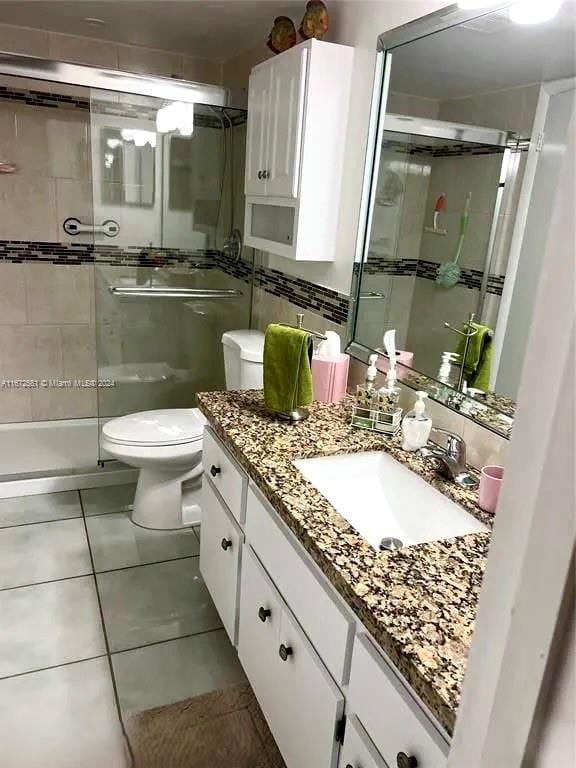 bathroom featuring vanity, toilet, tile patterned floors, and a shower with shower door