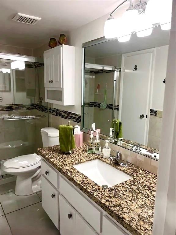 bathroom with vanity, toilet, a shower with shower door, and tile patterned flooring