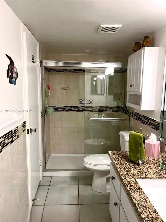 bathroom featuring vanity, a shower with shower door, toilet, and tile patterned flooring