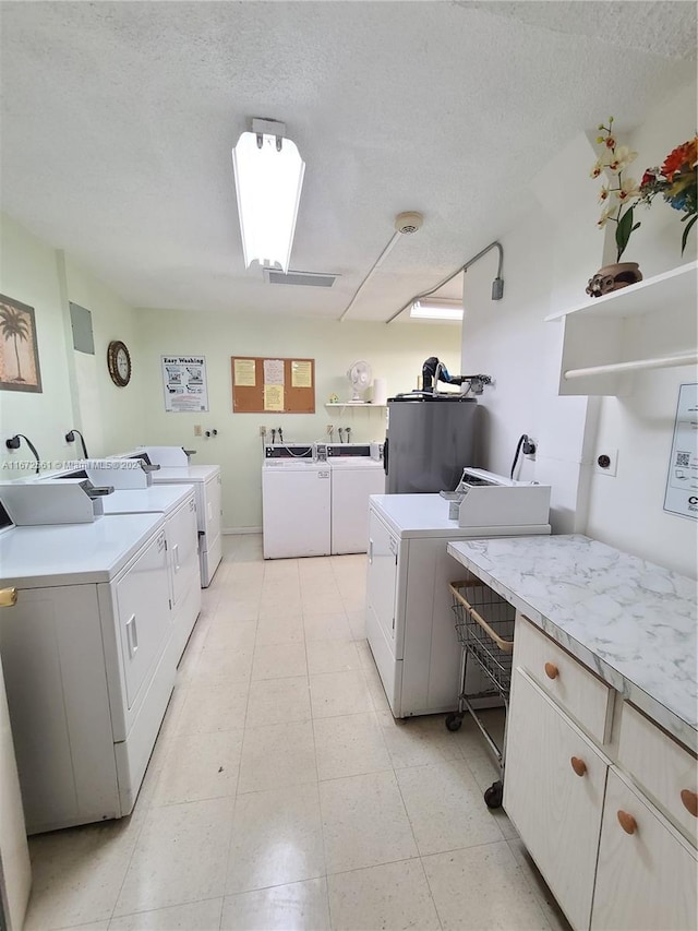 clothes washing area with water heater, washer and clothes dryer, and a textured ceiling