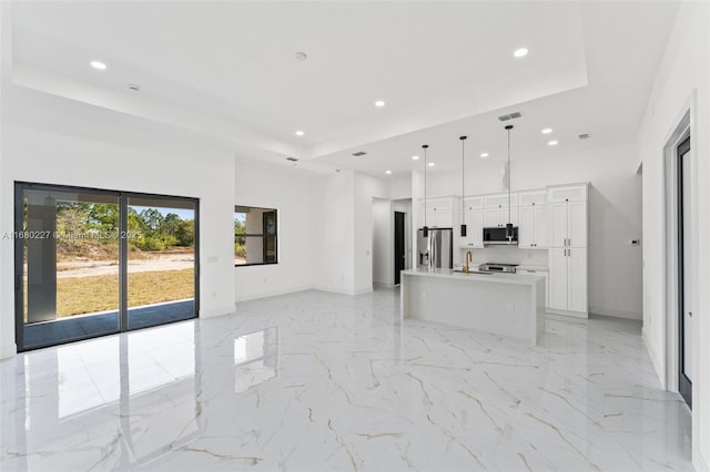 kitchen with appliances with stainless steel finishes, decorative light fixtures, an island with sink, white cabinets, and a raised ceiling