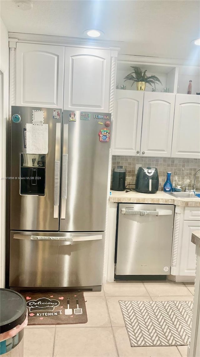 kitchen featuring stainless steel appliances, sink, light tile patterned floors, white cabinetry, and tasteful backsplash