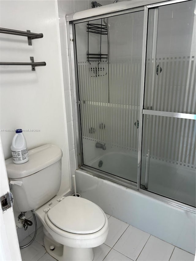 bathroom featuring toilet, tile patterned floors, and bath / shower combo with glass door