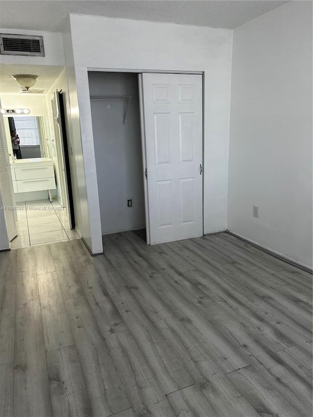 unfurnished bedroom featuring connected bathroom, a closet, a textured ceiling, and light wood-type flooring