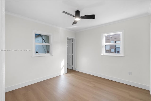 empty room featuring crown molding, light wood-style flooring, and baseboards