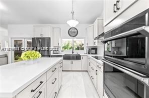 kitchen with stainless steel fridge, a kitchen island, white cabinetry, pendant lighting, and sink